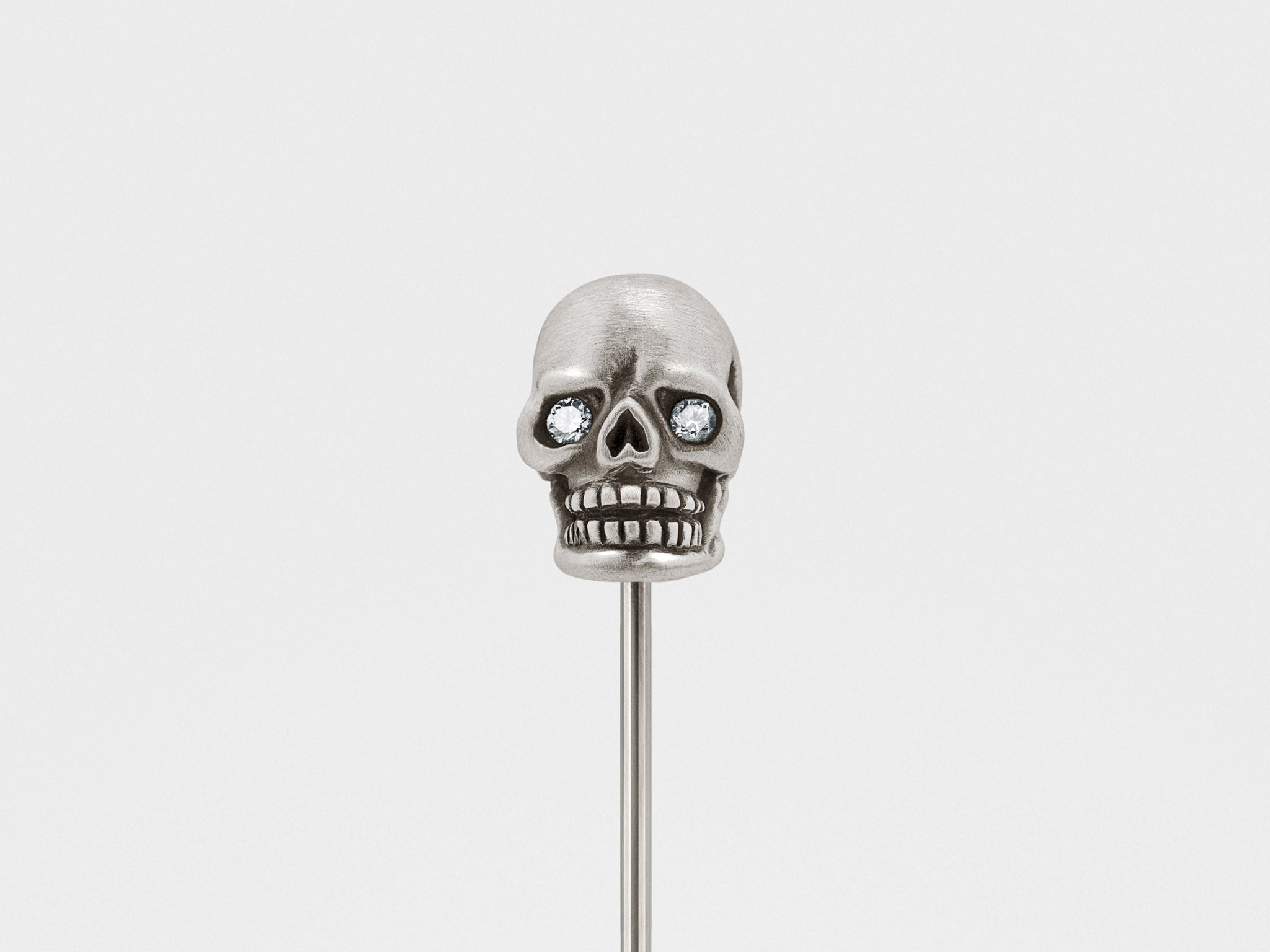 Pin de solapa de calavera en plata oscura con ojos transparentes